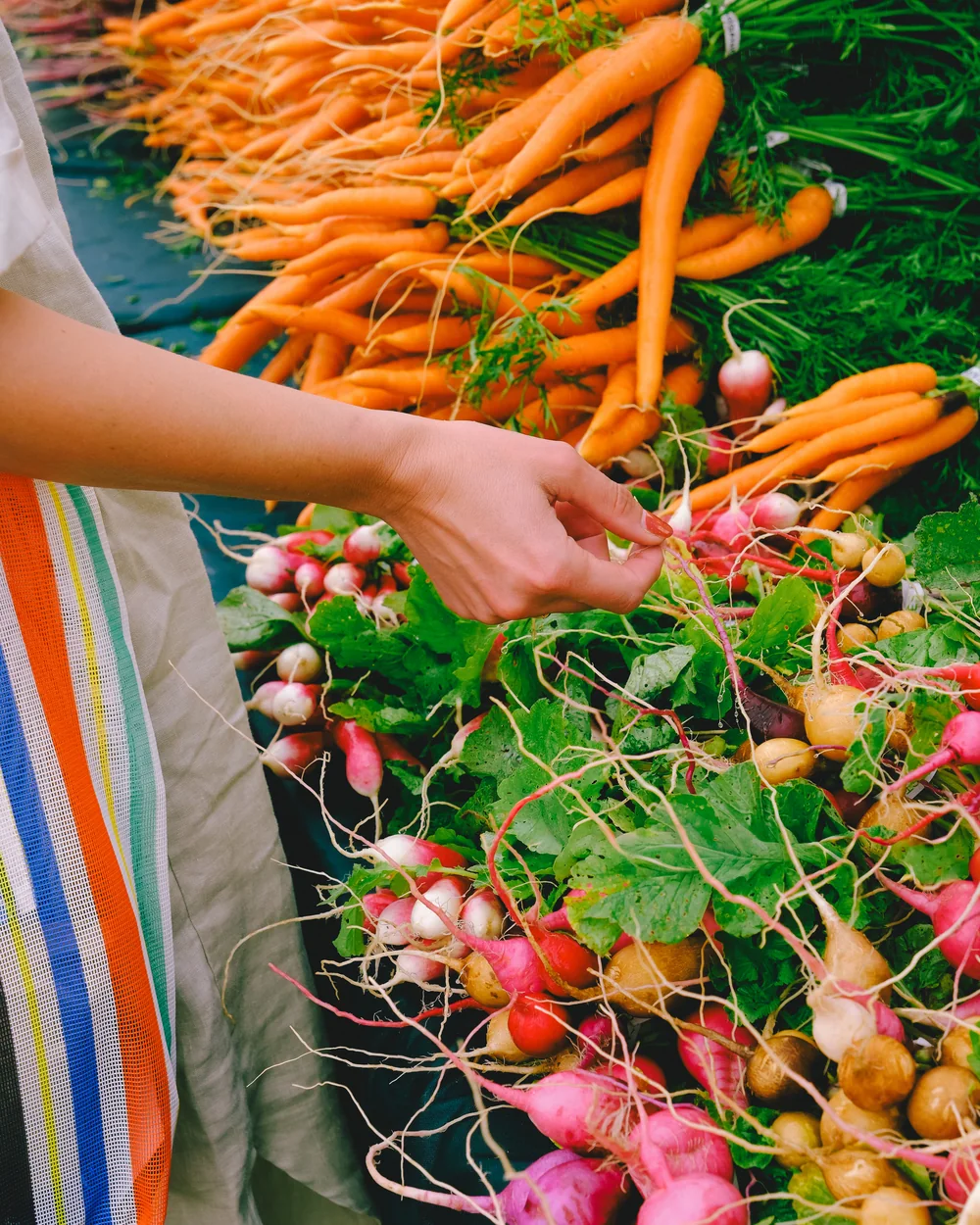 Choix des légumes sur un étal de marché, cabas rayé au bras