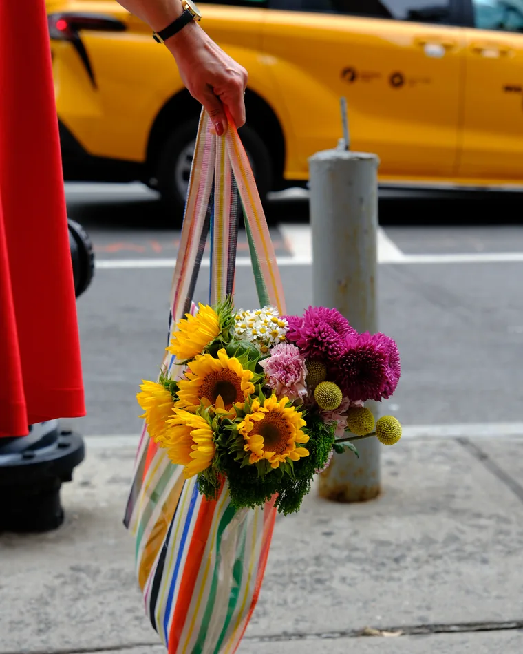 Cabas garni de fleurs porté sur un trottoir de New York, taxi jaune à l'arrière-plan