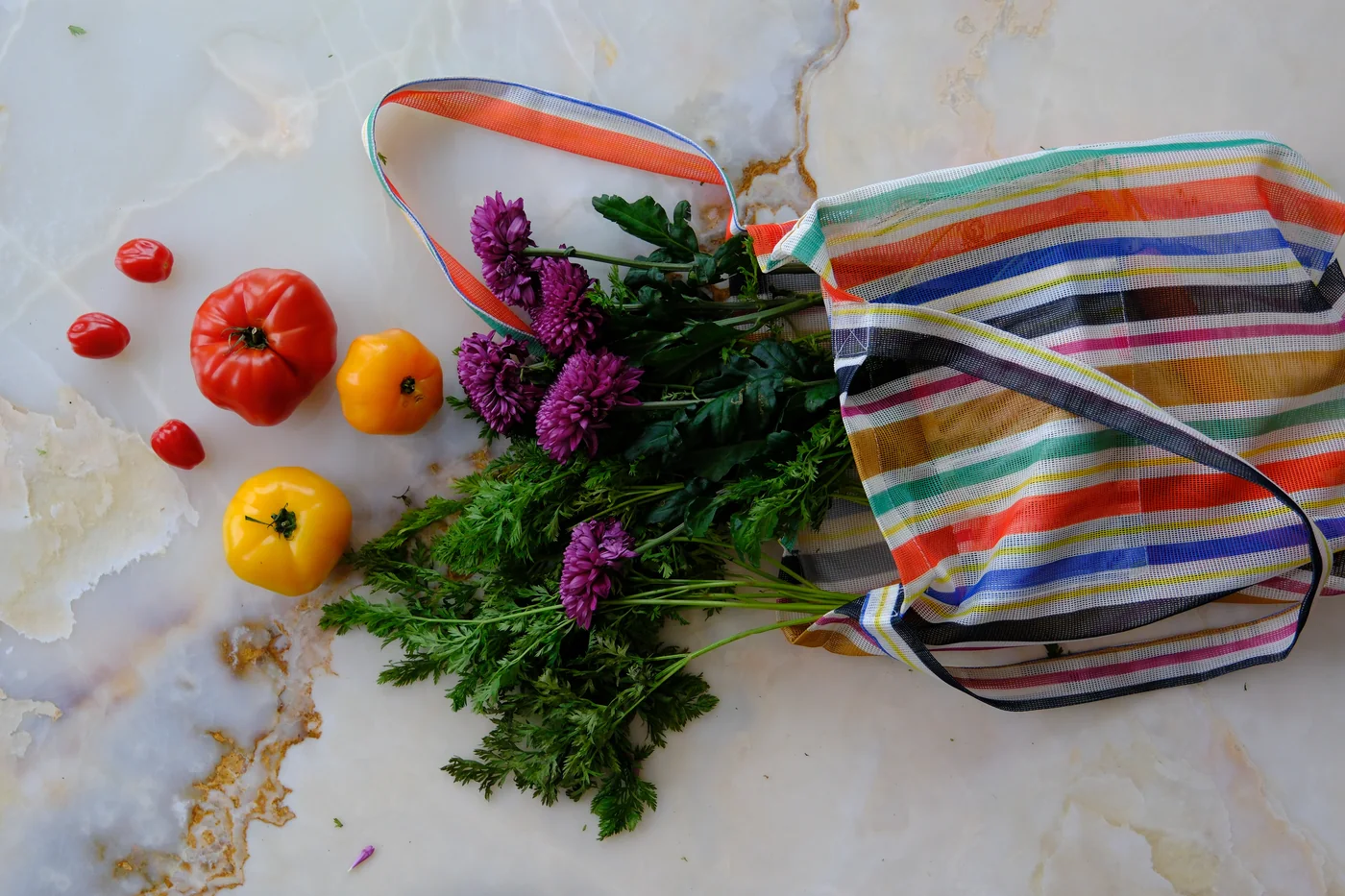 Nature morte sur plateau de marbre : tomates anciennes, fleurs et cabas rayé